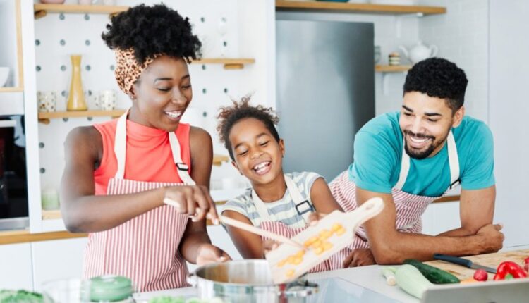 Two young adults and young child prepping vegetables at the kitchen counter.